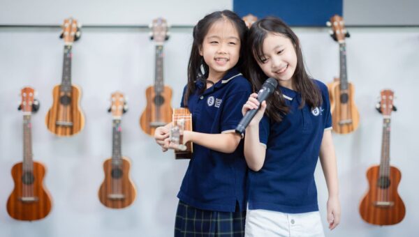 BASIS International School Bangkok students holding ukuleles beside an instrument rack